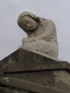 A weather-worn figure of a mourning girl on a tomb in New Orleans.